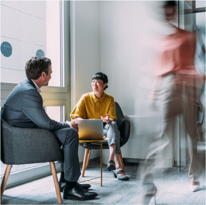 Business persons having a business meeting in office lobby while their colleagues are walking in blurred motion.