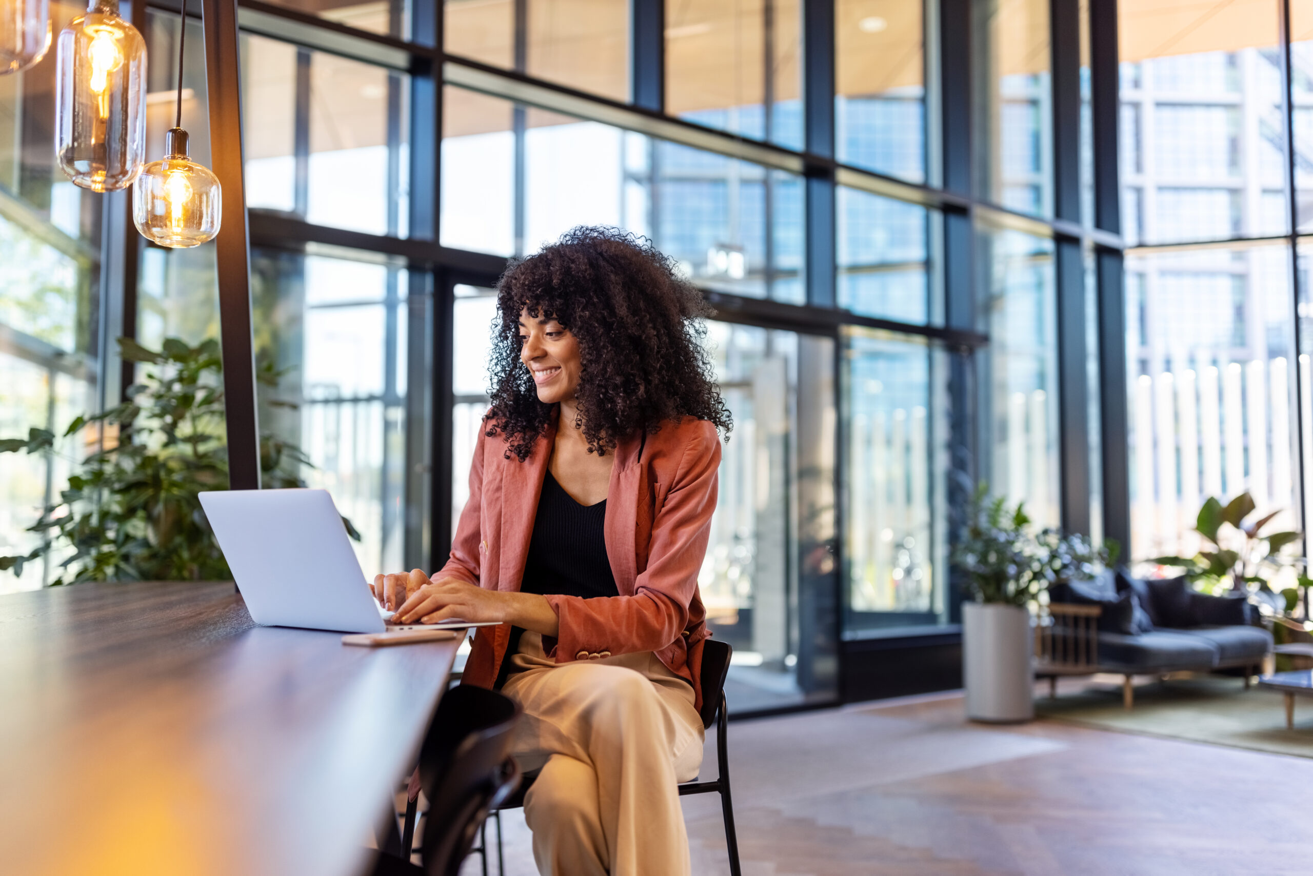 Young African woman working on laptop at office cafe. Happy female entrepreneur sitting in office lobby using laptop.