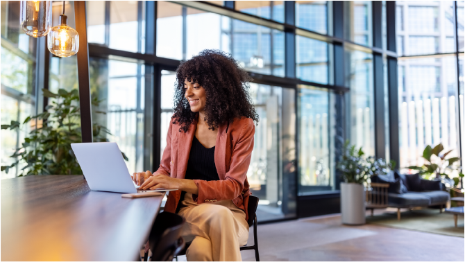 Young African woman working on laptop at office cafe. Happy female entrepreneur sitting in office lobby using laptop.