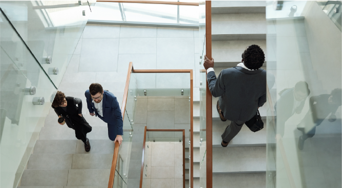 Overview of three young intercultural office workers in formalwear going upstairs while hurrying for work in the morning
