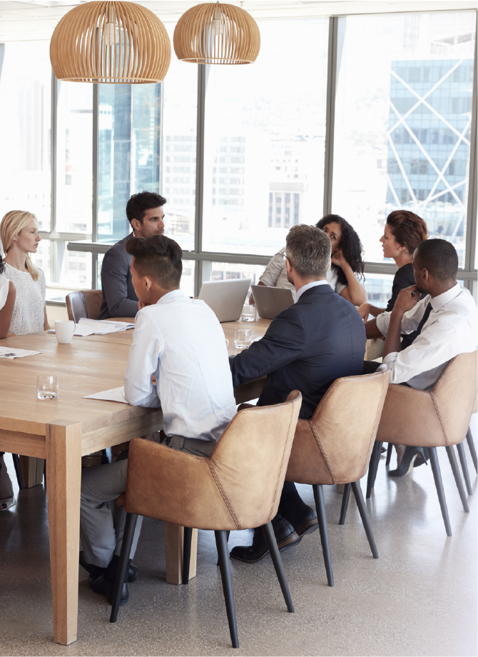 Group Of Businesspeople Sitting Around Table In Meeting Room