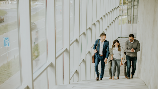 Group of corporate business professionals climbing the stairs in office corridor on a sunny day