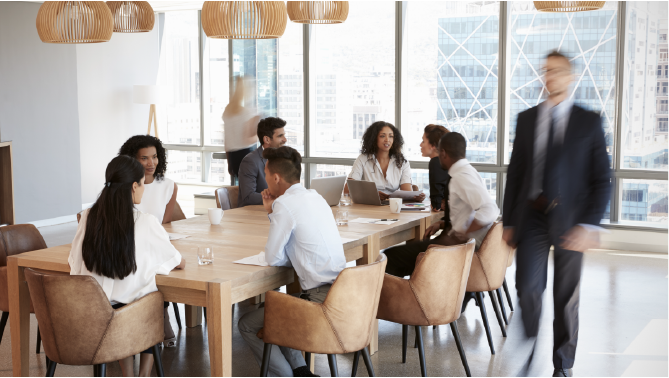 Group Of Businesspeople Sitting Around Table In Meeting Room