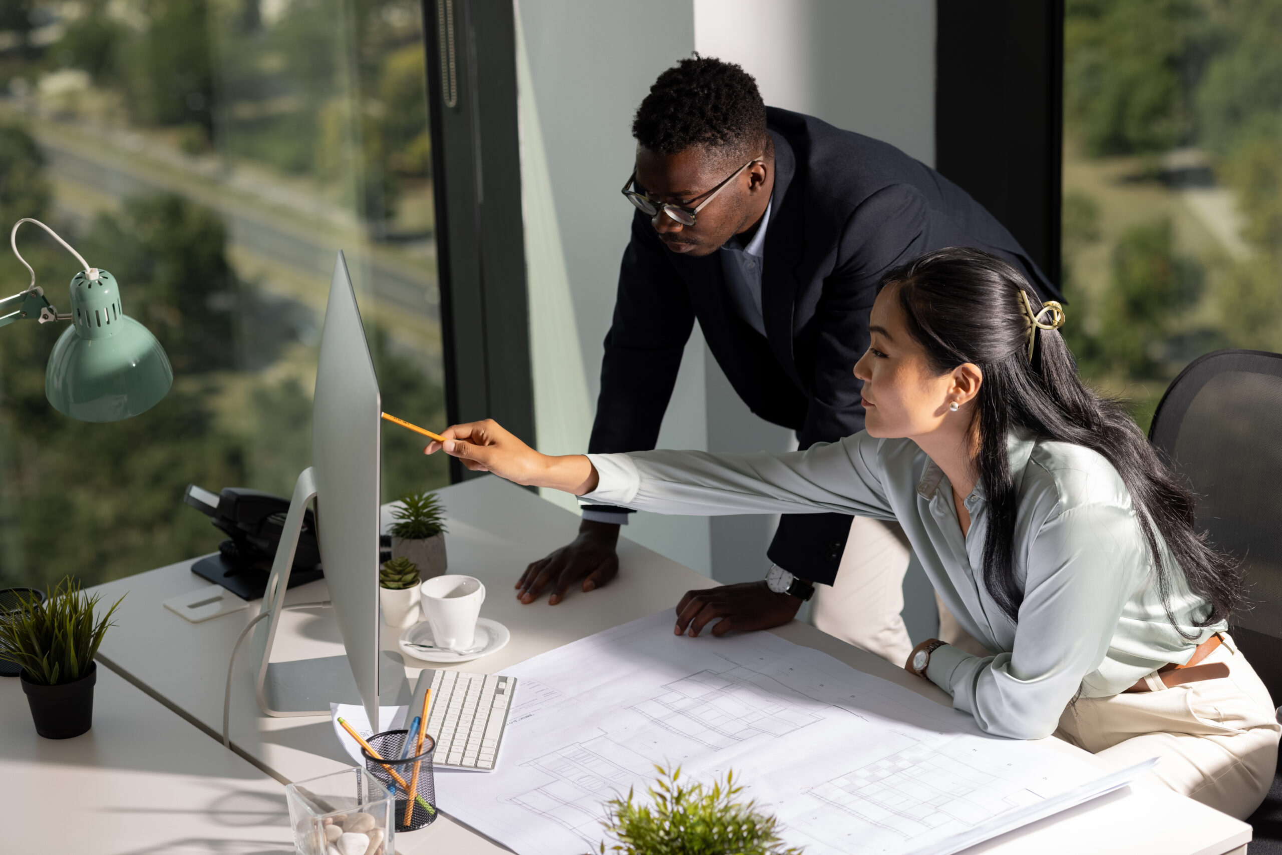 young African American man and his female colleague of Mongolian ethnicity working together as a team in their office, drawing some schematics and exchanging ideas.