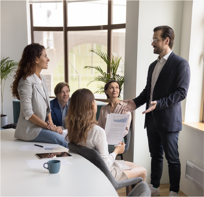 Confident businessman, male boss in suit explains new project details, share business strategy, makes speech stand in front of company staff members during corporate group briefing in conference room